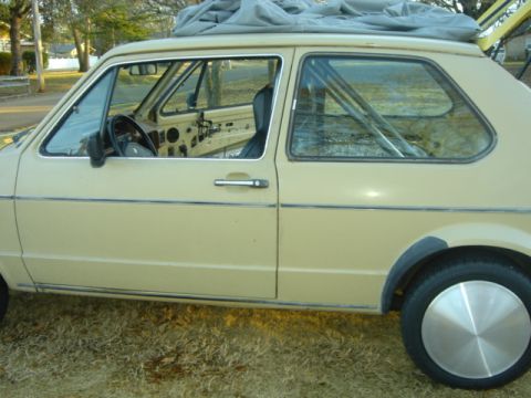 1983 Volkswagen Rabbit - Side view of a tan 1983 Volkswagen Rabbit, showing the interior roll cage and a car cover on the roof.