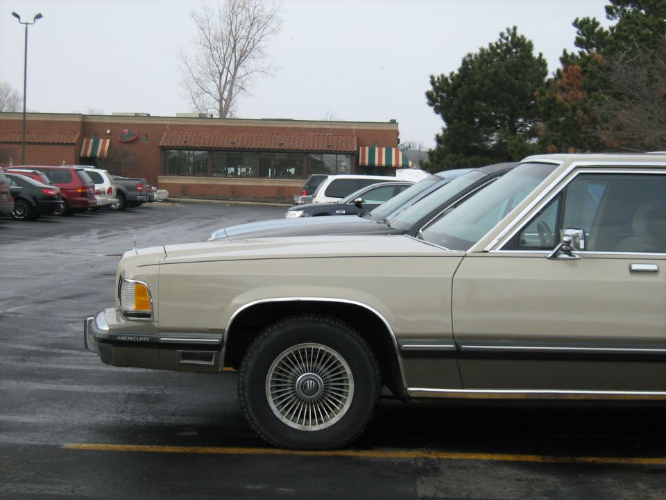 Tan 1988 Mercury Grand Marquis sedan parked on a wet asphalt lot, side view