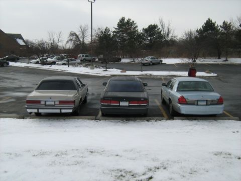 1988 Mercury Grand Marquis - Three sedans are parked in a lot covered with snow. The car on the right is a silver 1998 Mercury Grand Marquis.