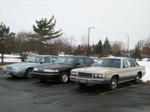 1988 Mercury Grand Marquis - Three sedans, including a tan 1988 Mercury Grand Marquis, are parked in an outdoor lot on an overcast day.