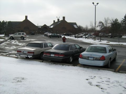 1988 Mercury Grand Marquis - Silver sedan, likely a 1998-2002 Mercury Grand Marquis, is seen from the rear in a snowy parking lot.