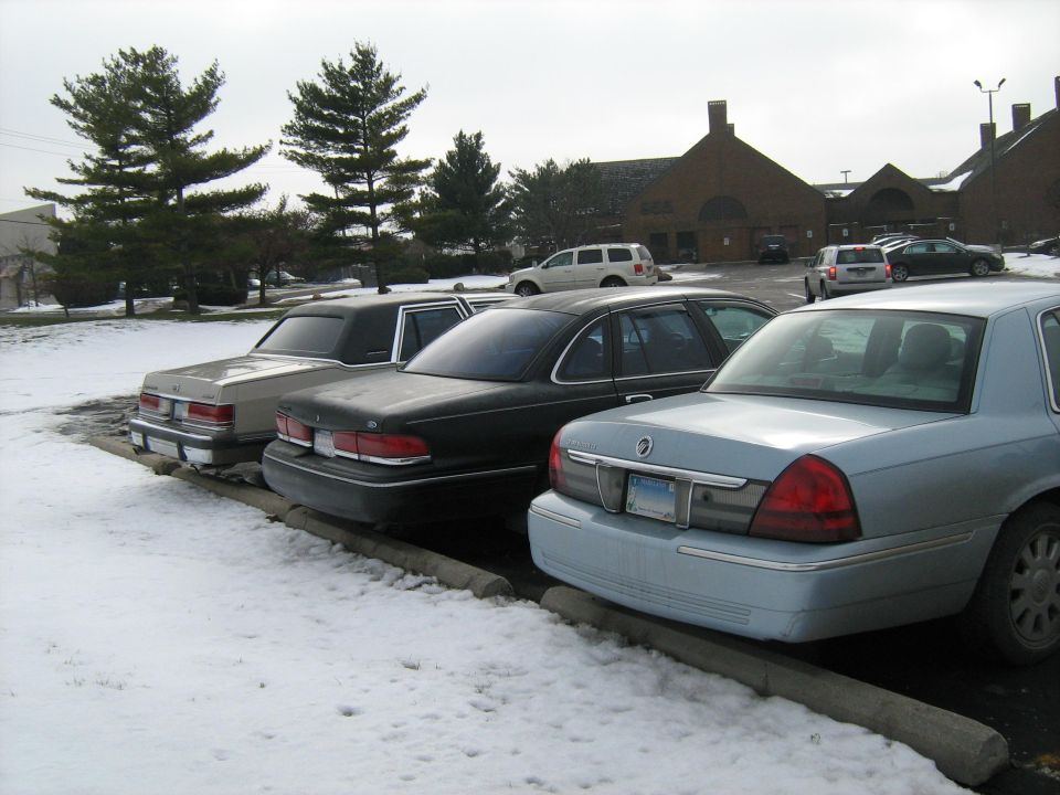 Three sedans parked in snow, one light blue, one black, and one beige. The light blue sedan is in the foreground