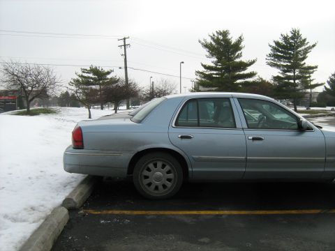 1988 Mercury Grand Marquis - A light blue sedan is parked in a lot during winter, with snow visible on the ground and trees in the background.