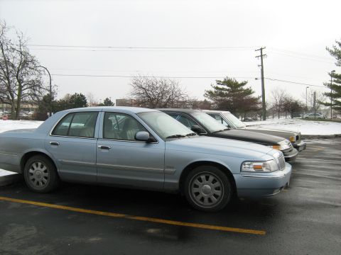 1988 Mercury Grand Marquis - A light blue sedan is parked in a lot next to other vehicles, with snow on the ground.