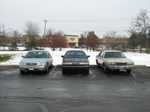 1988 Mercury Grand Marquis - Three sedans, including a 1988 Mercury Grand Marquis, are parked in a lot with snow on the ground.