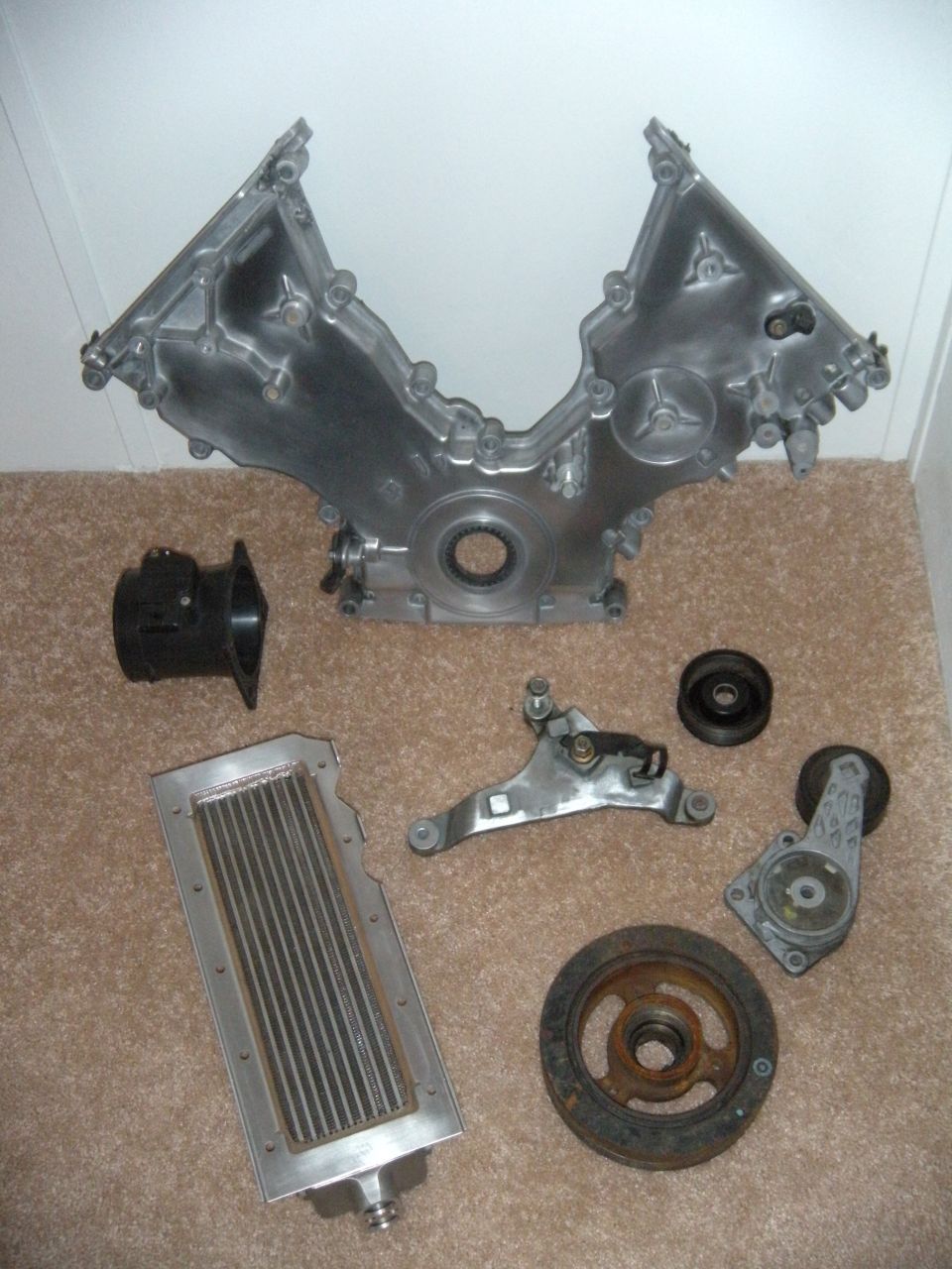 Engine timing cover, intake manifold, oil cooler, belt tensioner, and pulley assembly laid out on carpet
