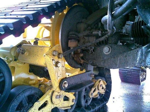 Yellow-framed rubber track conversion with drive sprocket and idler wheels on undercarriage