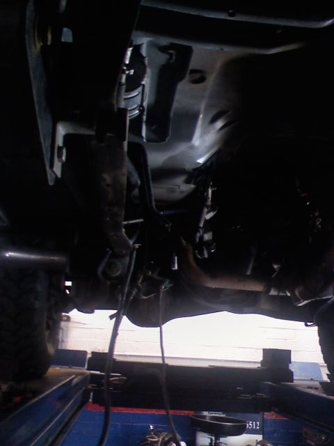 1996 Ford Bronco - The underside of a vehicle is viewed from below while it is raised on a lift.