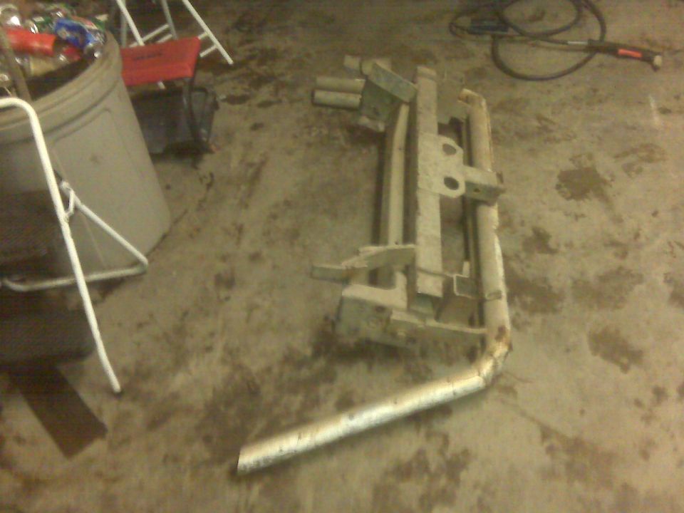 Metal truck bumper assembly with exhaust pipe attached, lying on concrete floor
