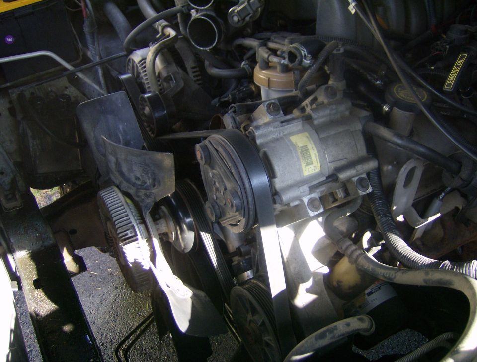 close-up of engine components including belts, pulleys, and AC compressor