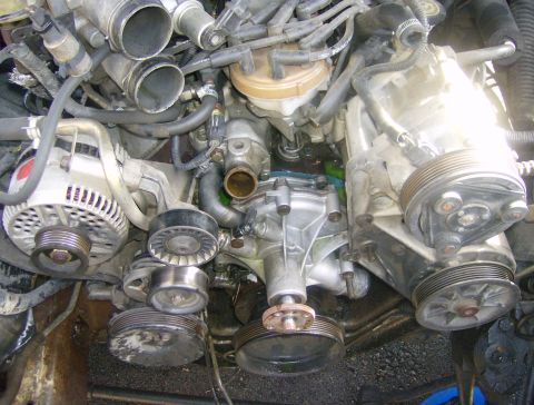 1994 Ford Bronco - Close-up view of the engine bay, highlighting the alternator, various pulleys, and the water pump assembly.