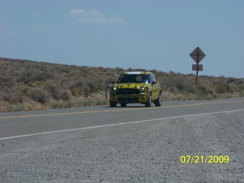 2009 Kenworth T800 - A yellow Mini Countryman prototype drives down a highway, its camouflage wrap partially obscuring its design.