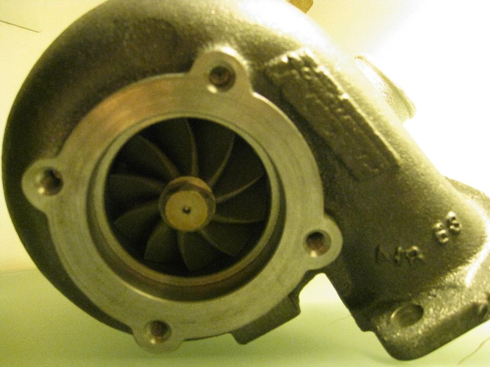 Turbocharger compressor housing with visible impeller blades and mounting holes. Part numbers are stamped on the housing