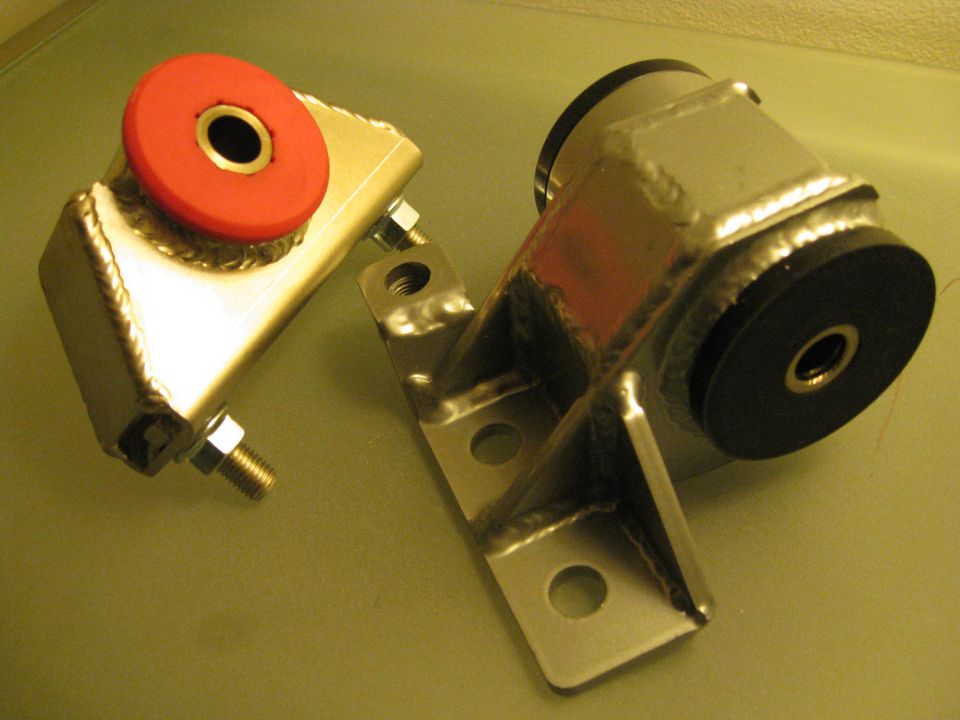 Two aftermarket engine mounts, one with a red bushing, the other with a black bushing