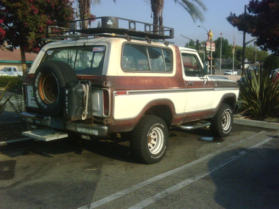 Two-tone brown and white Ford Bronco with a roof rack and spare tire on the back