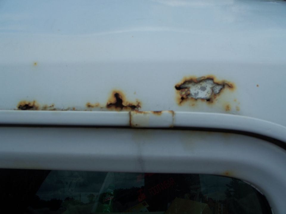 Close-up of rust spots forming on the white paint above a vehicle's window trim