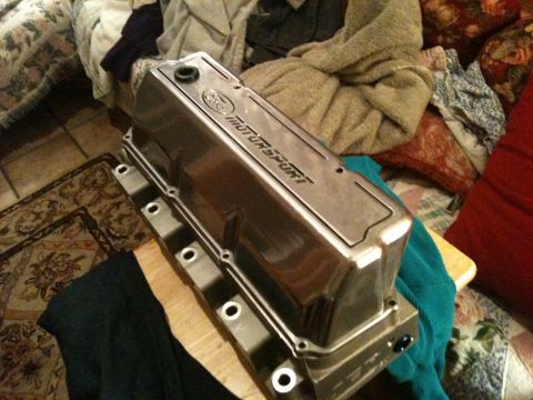 1972 Ford Ranchero - A polished cast-aluminum Ford Motorsport tall valve cover sits on a wooden stool indoors, its raised 'MOTORSPORT' script and Ford oval logo…