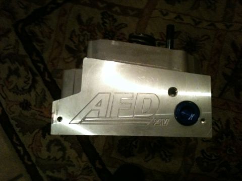 1972 Ford Ranchero - A bare aluminum cylinder head sitting on a patterned rug, its side face engraved with the "AFD" logo and "2V" marking, with a blue anodized…
