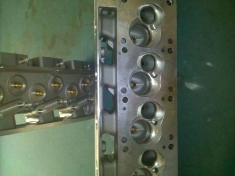 1972 Ford Ranchero - Two freshly rebuilt aluminum cylinder heads stood on a green-painted bench, the near one showing its machined deck surface with four wedge…