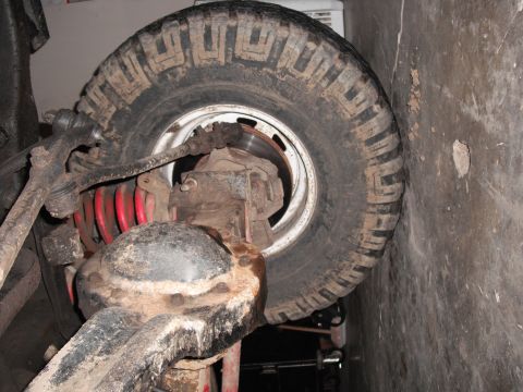 1991 Ford Bronco - The underside of a vehicle shows the rear axle, red coil springs, and a dirty tire.