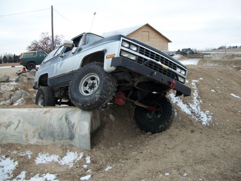 1989 Ford Bronco - This modified SUV is attempting to climb over a concrete obstacle on a dirt mound.