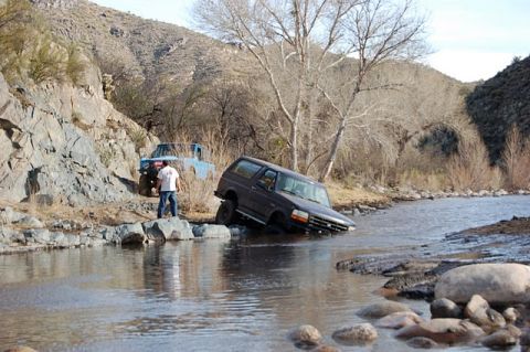 1996 Ford Bronco - Two off-road vehicles navigate a rocky riverbed in a dry, mountainous landscape.