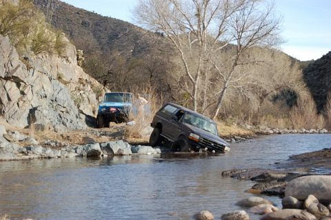 1996 Ford Bronco - A 1996 Ford Bronco is partially submerged in a river while another SUV climbs a rocky bank.
