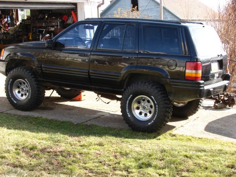 1996 Jeep Grand Cherokee - A black 1996 Jeep Grand Cherokee is shown with a lifted suspension and large off-road tires, parked in front of a garage.