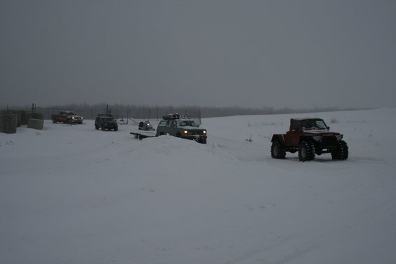 Several off-road vehicles drive through a snowy field under a gray sky