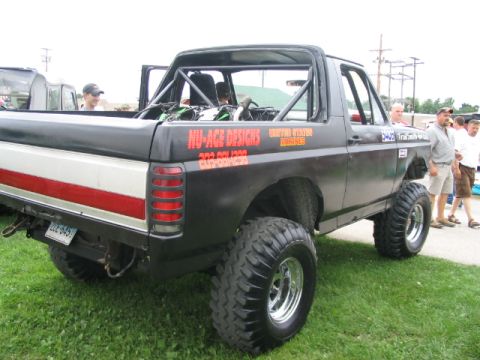 1986 Ford Bronco - A heavily modified Ford Bronco with large off-road tires and a roll cage is parked on grass.