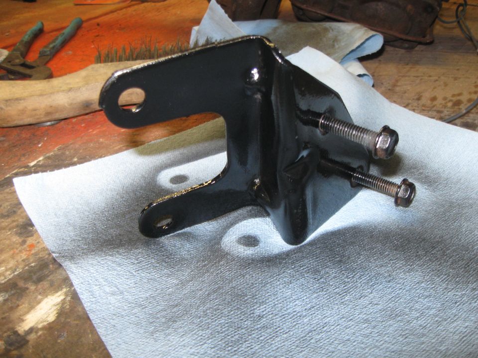 Black metal bracket with two bolts, resting on paper towels