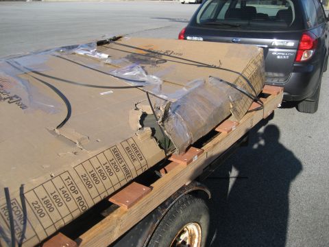 1996 Ford Bronco - A large, damaged cardboard box is strapped to a trailer, towed by a Subaru Outback.