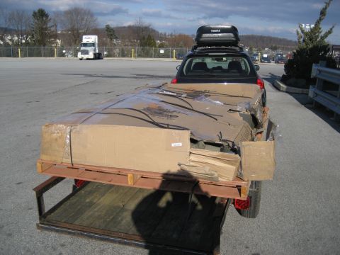 1996 Ford Bronco - A car tows a trailer filled with large, damaged cardboard boxes in a parking lot.