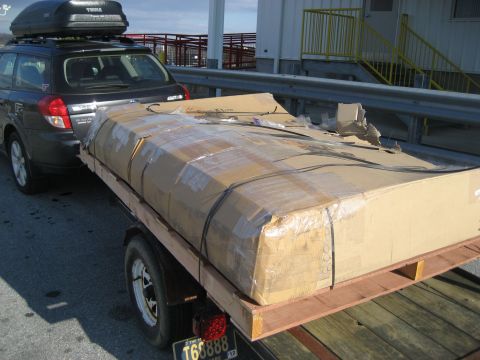 1996 Ford Bronco - A dark SUV tows a trailer carrying a large, taped cardboard box, with a roof rack on top.
