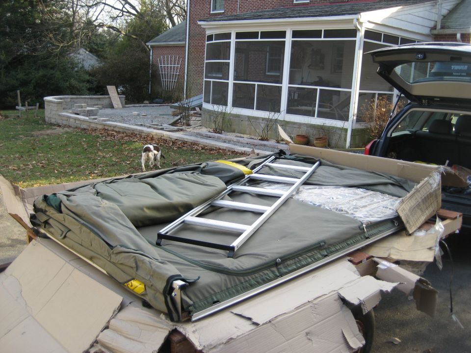 Tent and ladder being loaded into a car's open trunk