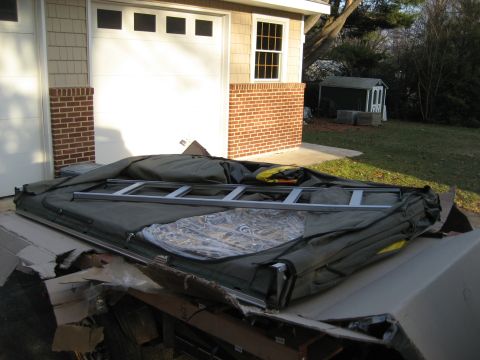 1996 Ford Bronco - A folded rooftop tent and ladder are stored on a vehicle in front of a garage.