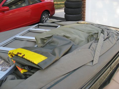 1996 Ford Bronco - A red car is parked next to a folded tent and stacked tires in front of a garage door.