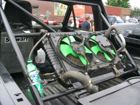 1986 Ford Bronco - A modified truck's interior shows a large radiator with green fans, a fire extinguisher, and a roll cage, with other vehicles visible outsi…