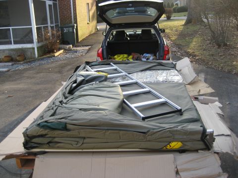1996 Ford Bronco - A folded tent and ladder are laid out on cardboard, positioned next to an SUV with its rear hatch open.