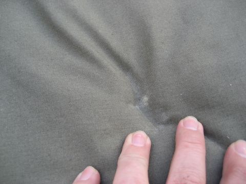 1996 Ford Bronco - Close-up of a textured olive green fabric with a small blemish, touched by fingers.