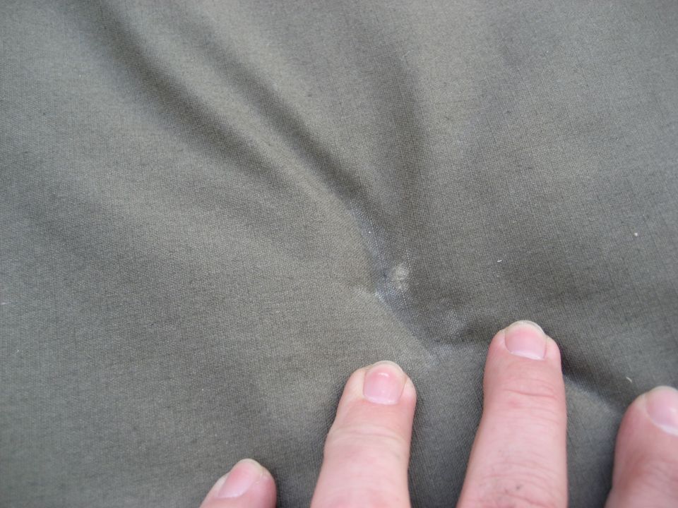 fingers touching a wrinkled olive green fabric with a small light spot