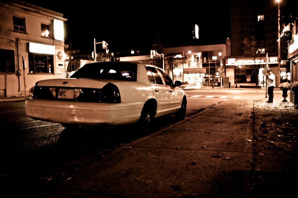 White Ford Crown Victoria parked at a city curb at night, low rear three-quarter angle