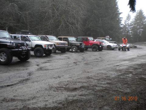 2005 Jeep Wrangler - A group of off-road vehicles, including Jeep Wranglers, are parked on a muddy lot with an ATV and rider present.