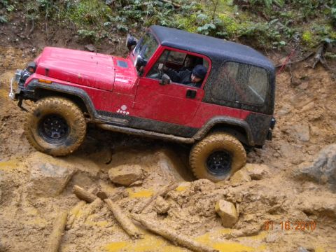 2005 Jeep Wrangler - A red Jeep Wrangler tackles a challenging muddy terrain with its tires deep in the muck.