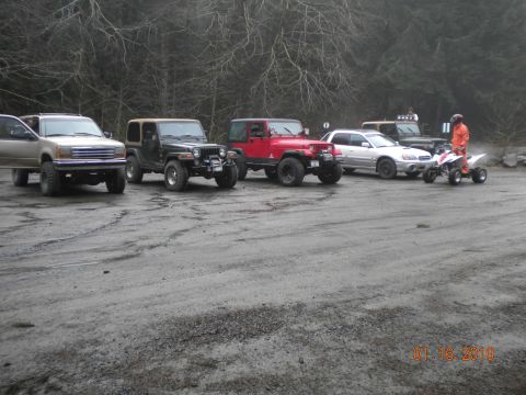 2005 Jeep Wrangler - A collection of Jeeps, an SUV, a sedan, and an ATV are parked in a lot on a cloudy day.