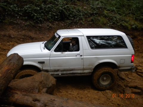 2005 Jeep Wrangler - A white Ford Bronco is shown off-roading on a muddy trail with large logs.