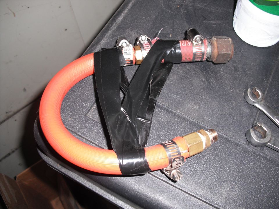 Improvised hose adapter made from an orange hose, black tape, and metal fittings. Two wrenches are visible nearby