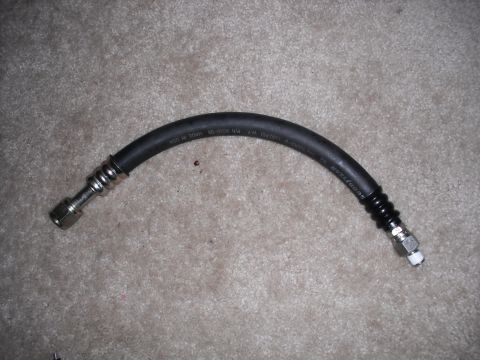 1991 Ford Bronco - A black automotive hose with metal fittings and ribbed protective sleeves is shown against a carpeted background.