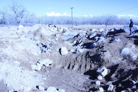 1989 Ford Bronco - A person surveys a rough terrain area with debris and dirt mounds under a clear sky.