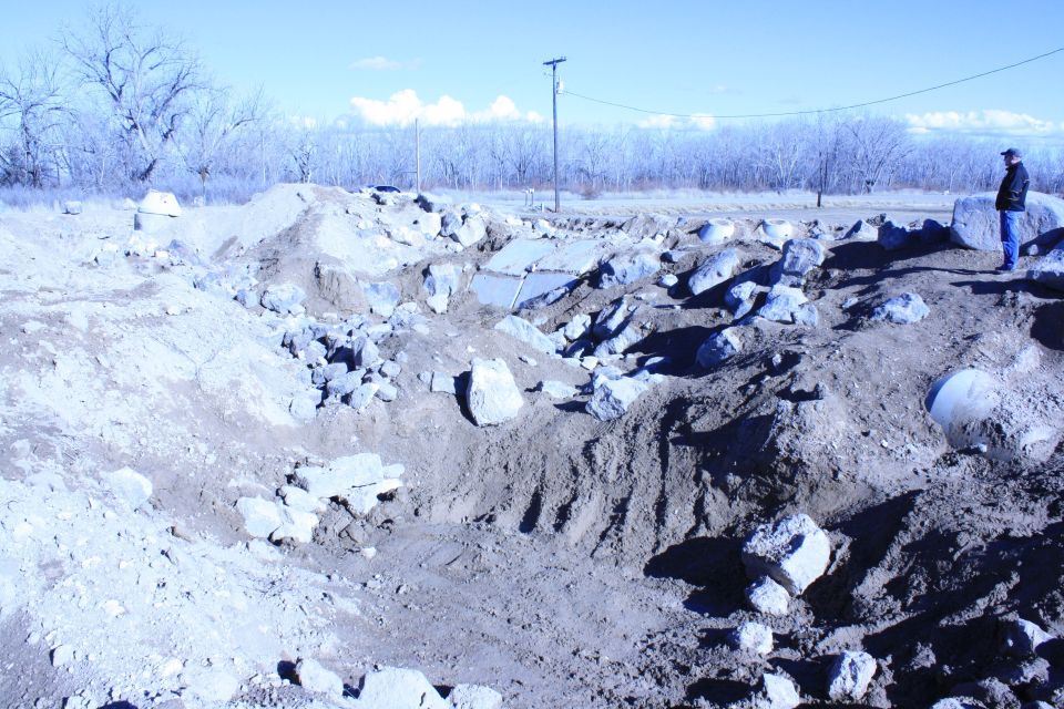 Construction site with piles of dirt and rocks, a person stands on a mound in the background